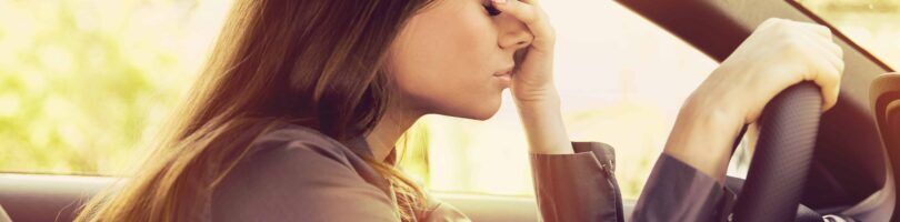 women at wheel holding head from fatigue
