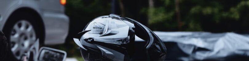 A motorcycle accident scene with a helmet on road with car parked in background