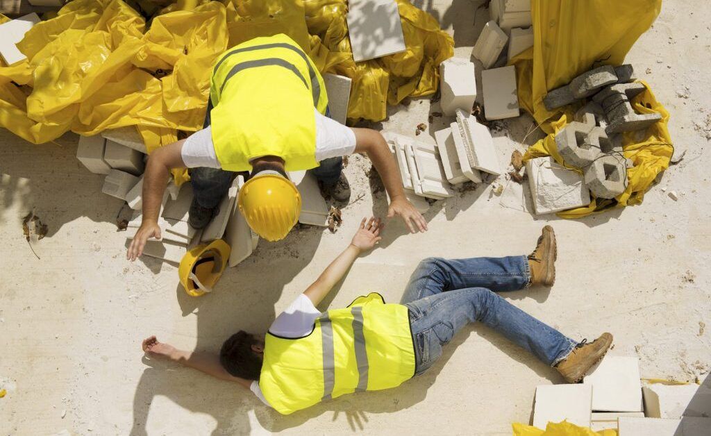 construction worker on ground unconscious with coworker trying to help